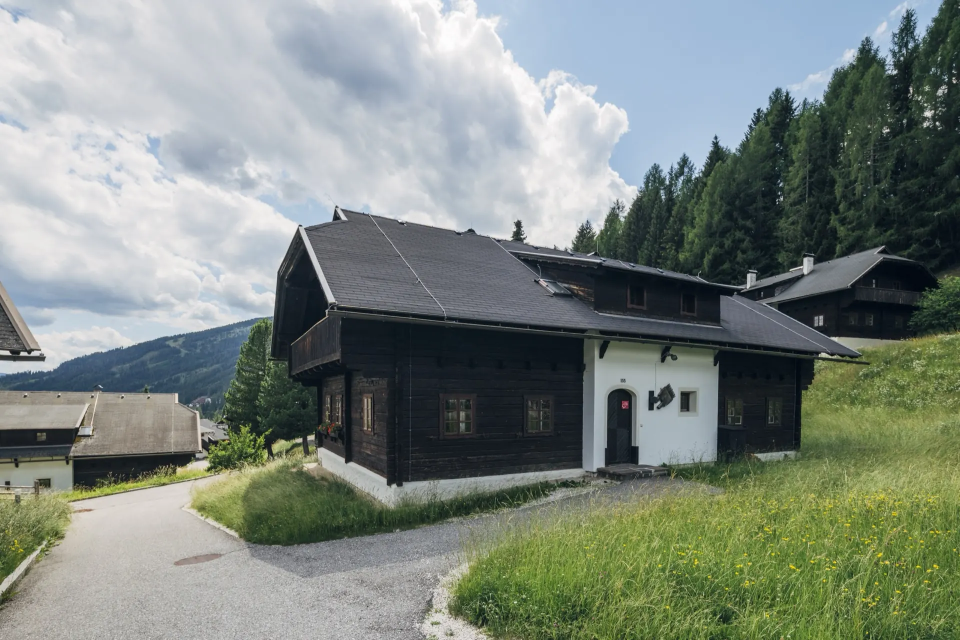 Holzhaus mit weißem Sockel am Dorfweg im Sommer