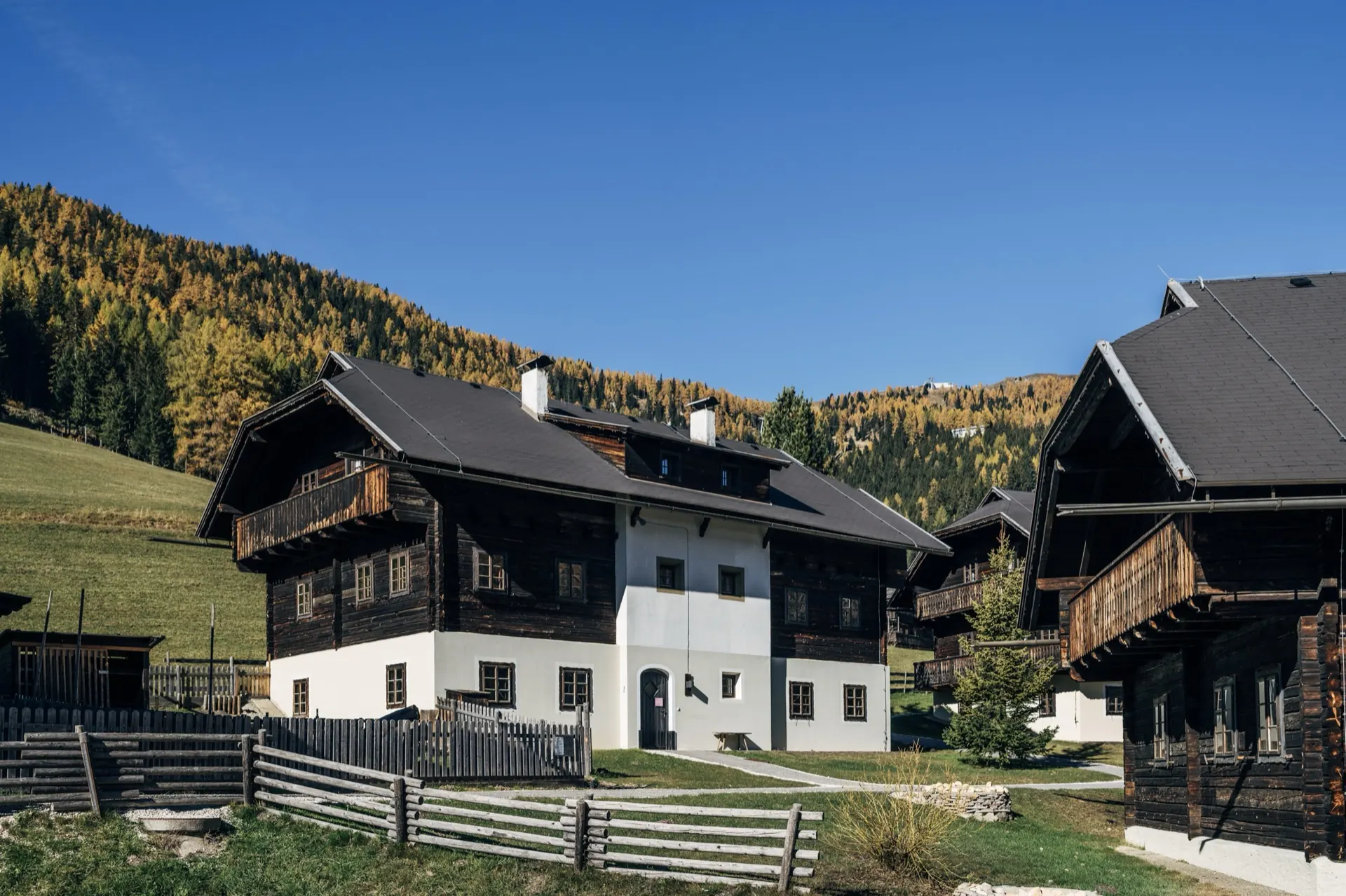 Holz- und Steinhäuser im Dorf vor herbstlich gefärbtem Lärchenwald