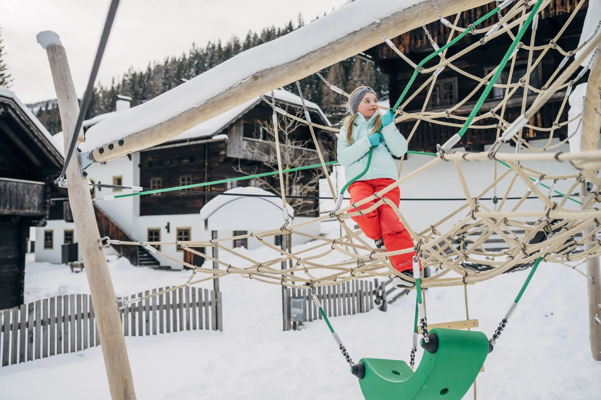 Mädchen klettert im verschneiten Seilnetz des Spielplatzes