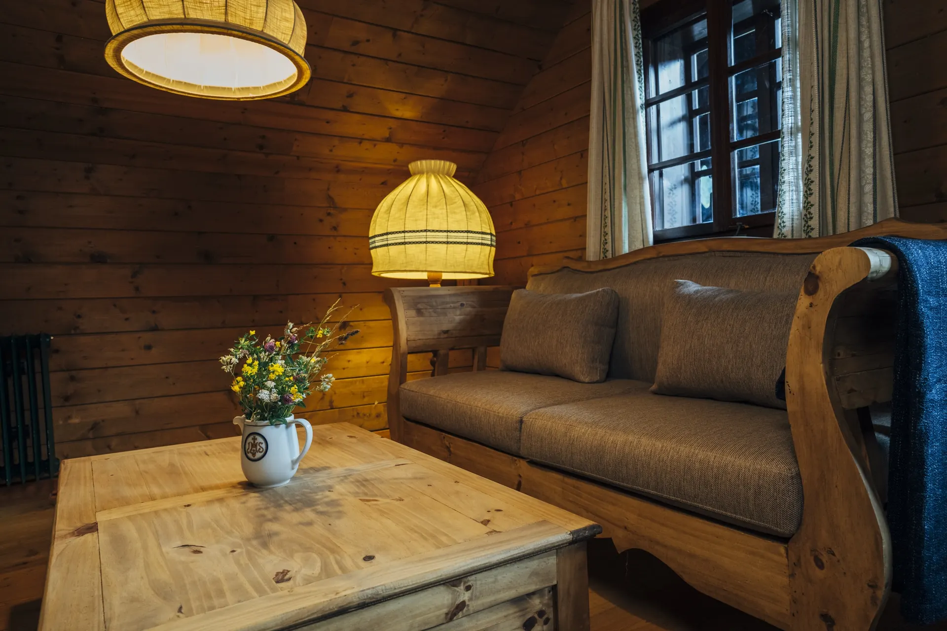 Stube der Kolmnock-Wohnung mit Sofa, Holztisch und Lampe