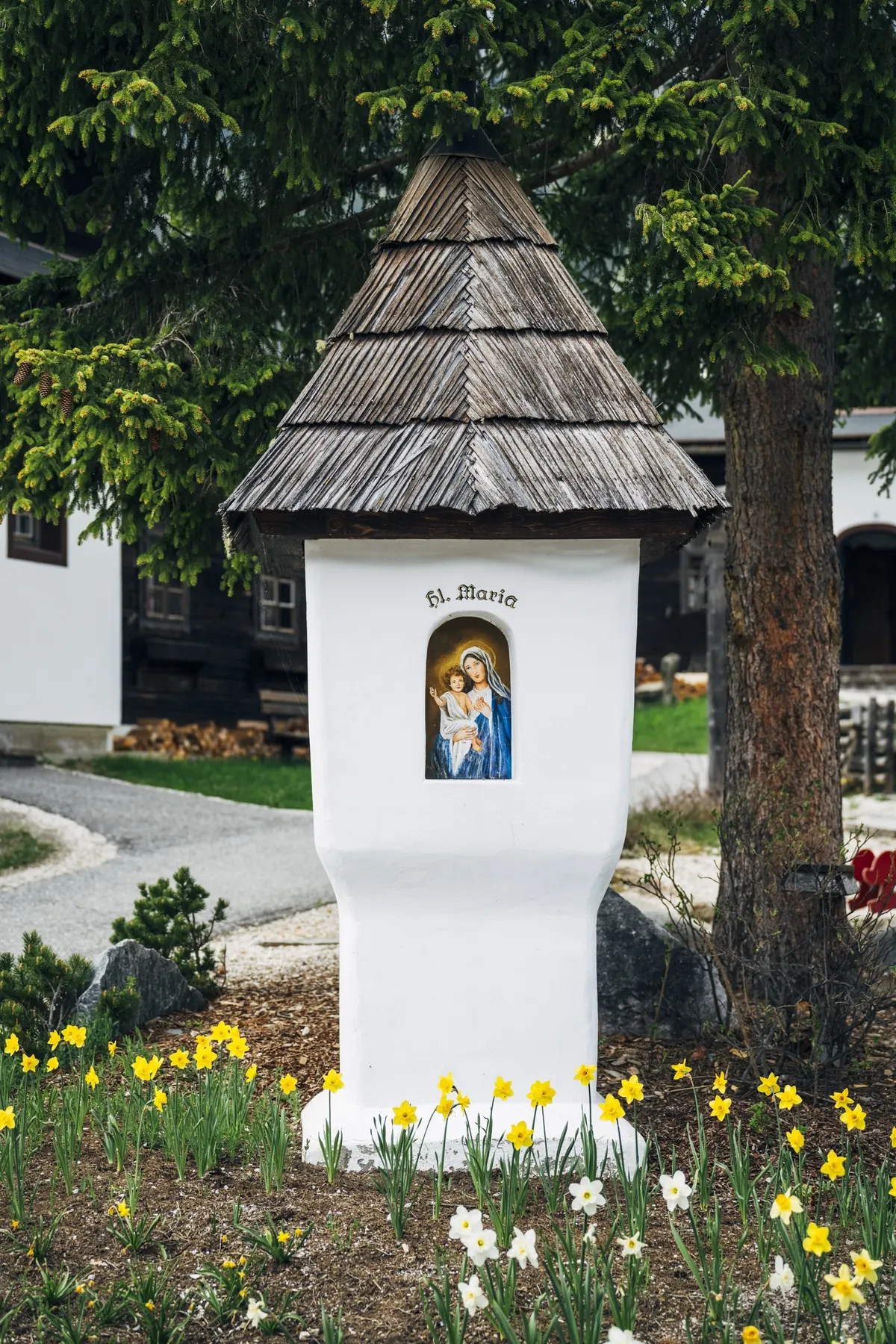Bildstock mit Narzissen vor dem Holzhaus