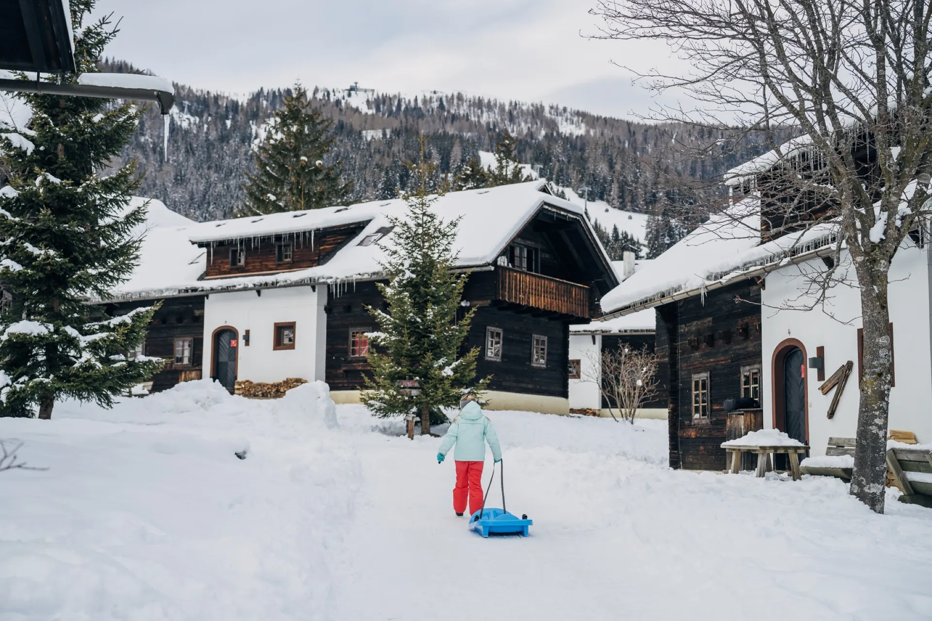 Kind mit Schlitten vor dem verschneiten Haus