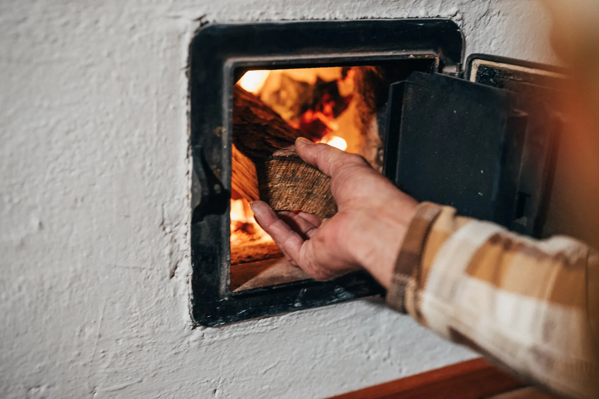 Holzscheit wird in den Kachelofen geschoben