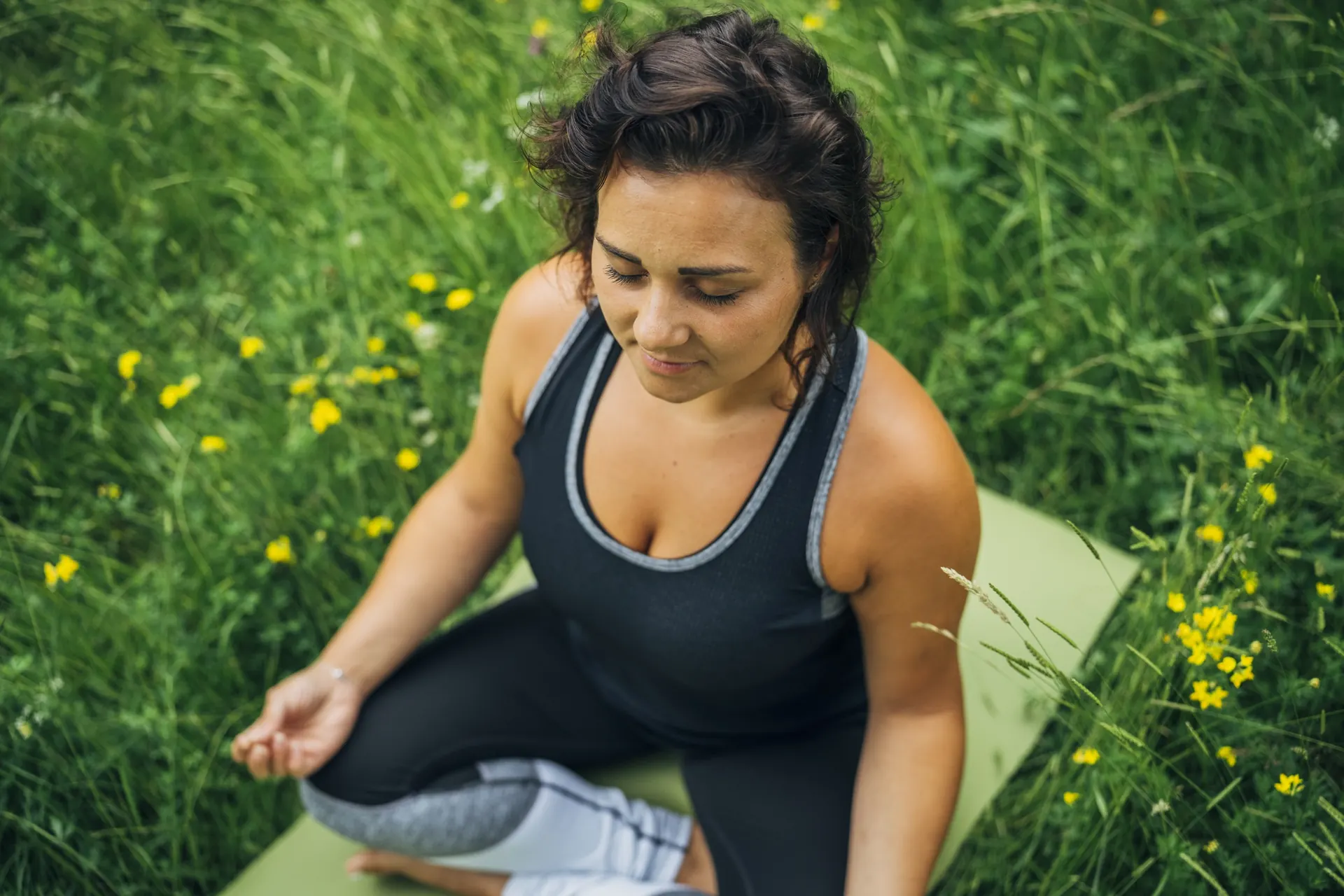 Frau sitzt mit Yogamatte in der Blumenwiese