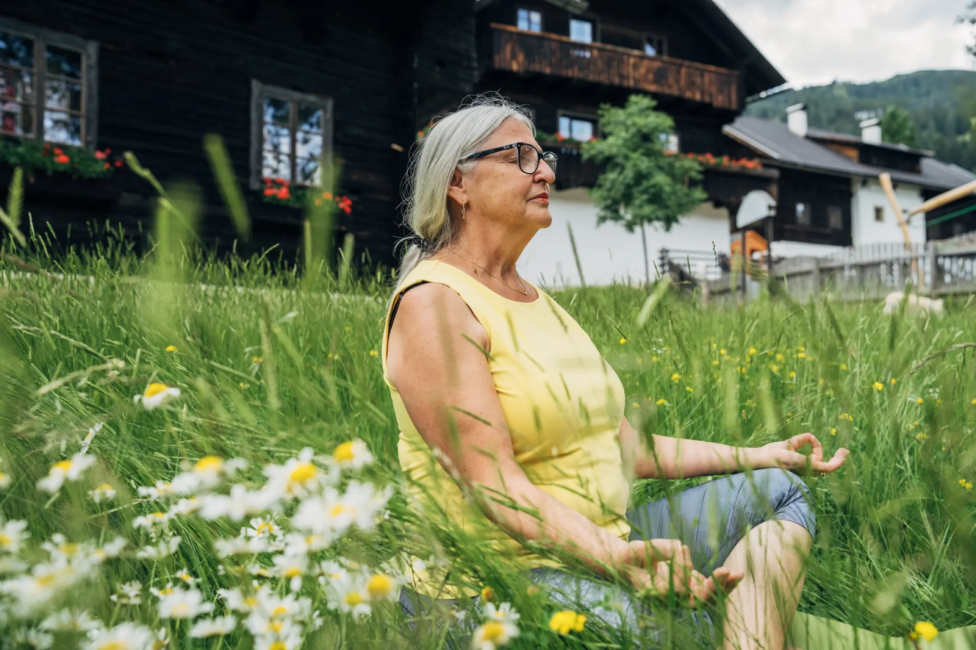Frau beim Yoga in der Blumenwiese vor dem Holzhaus