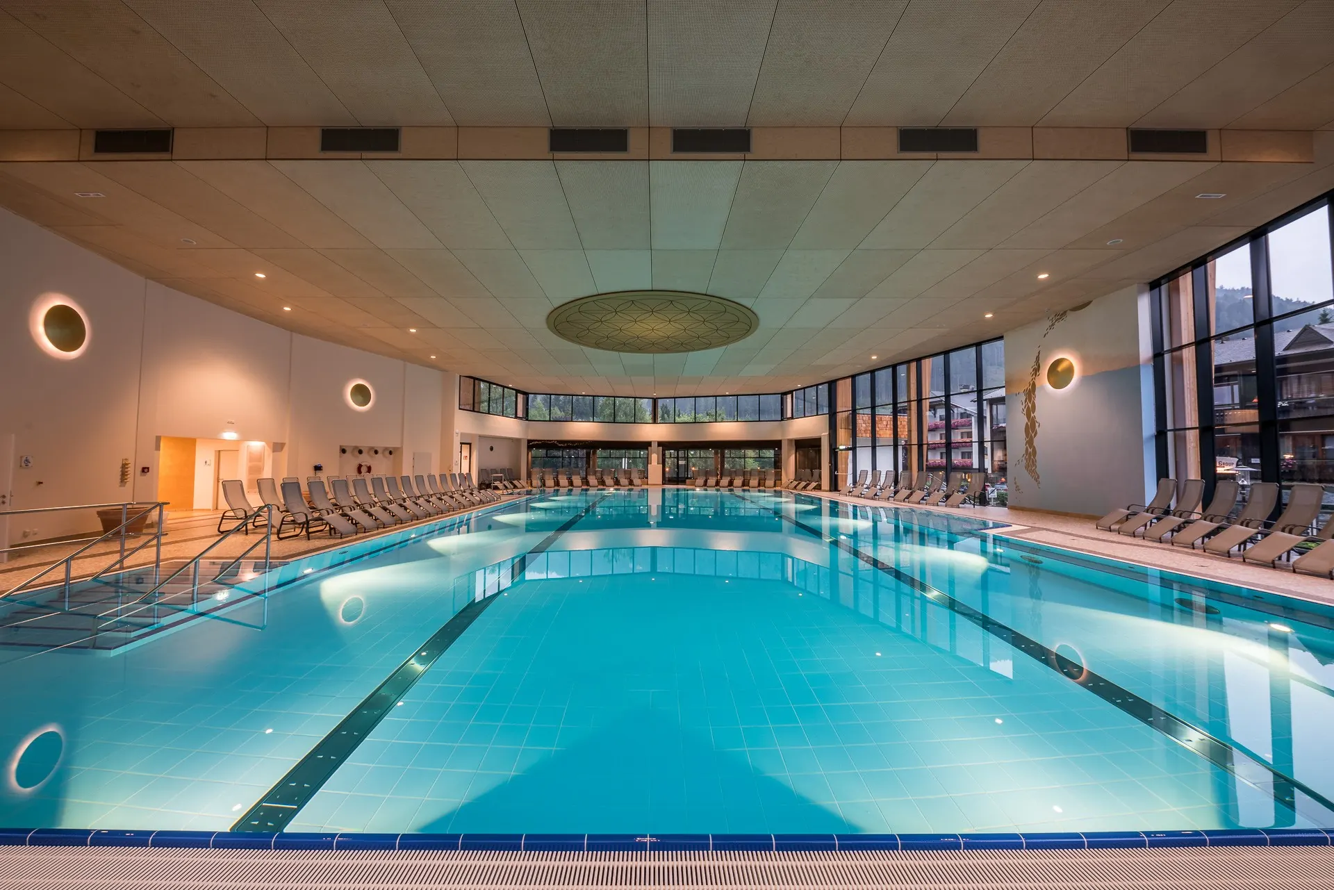 Thermenhalle mit großem Becken, Holzdecke und Glasfront zu den Bergen