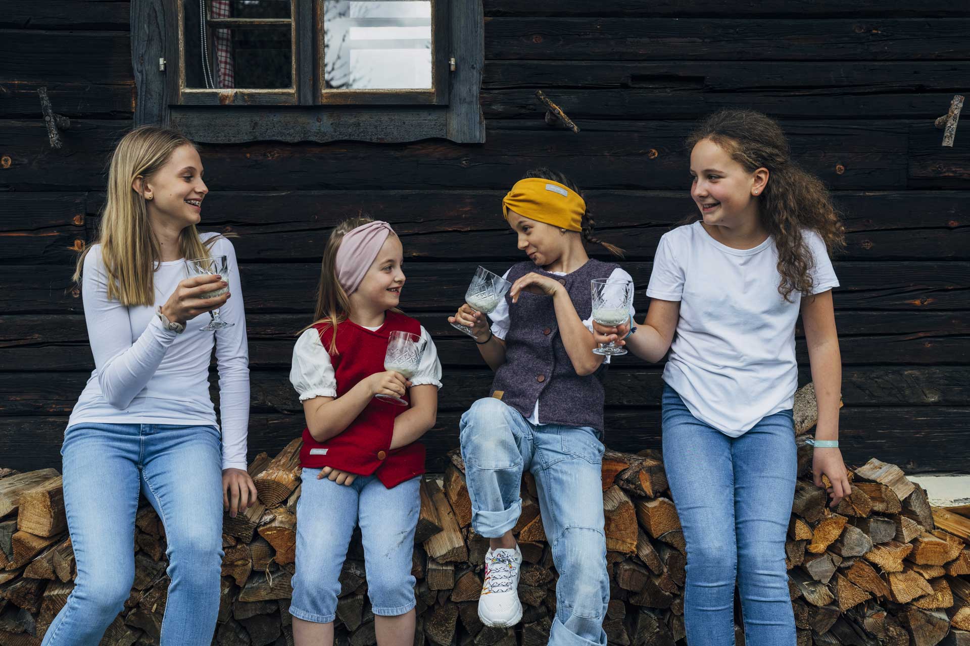 Ferienwohnungen für den Familienurlaub in Kärnten | Slow Travel Resort Kirchleitn | Kinder trinken frische Bio-Milch vom regionalen Bauern und sitzen auf Holzscheiten