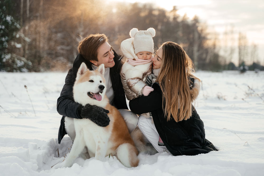Familie sitzt im Schnee beim Winterurlaub mit Kleinkind und Hund in Kärnten
