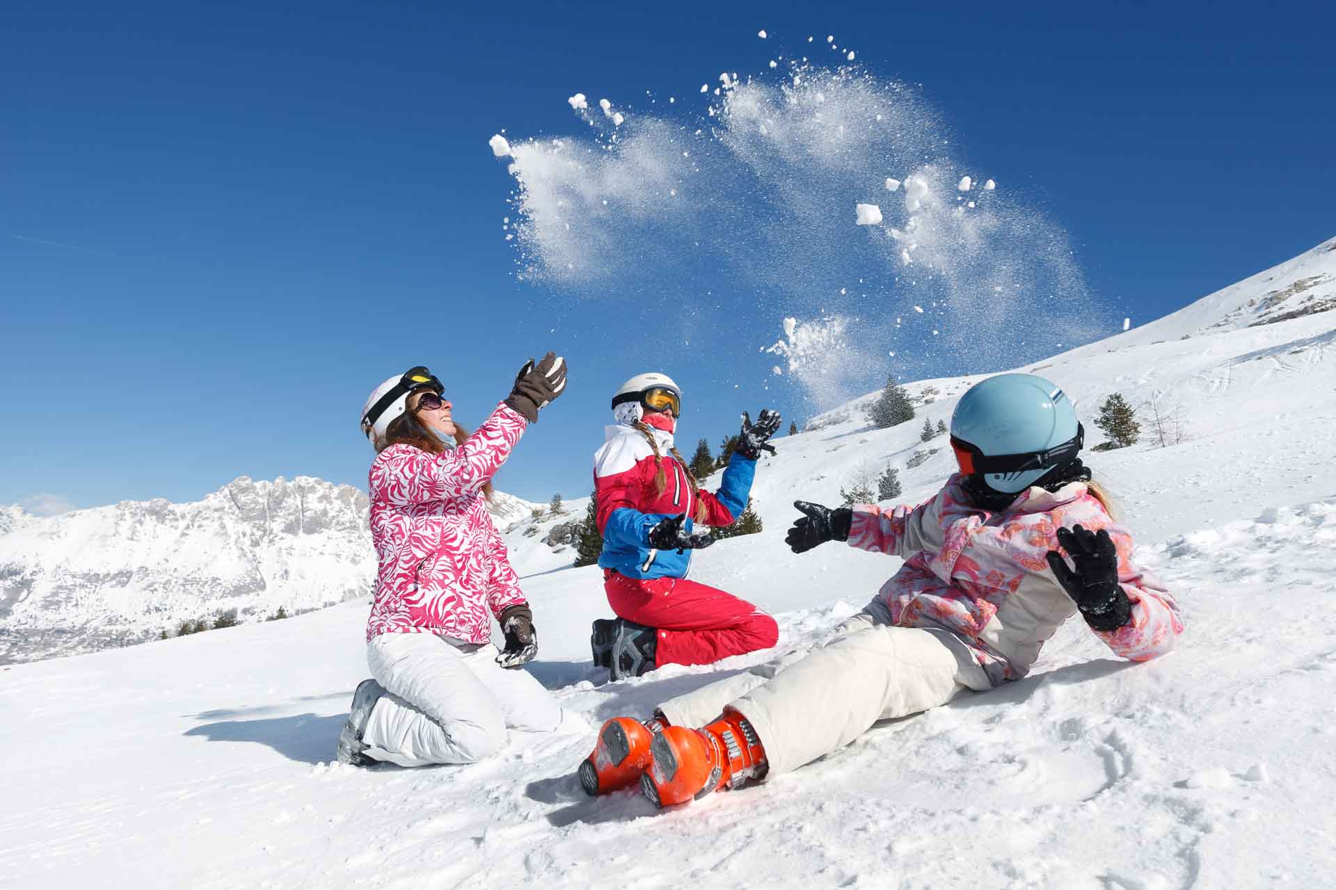Skiurlaub in Bad Kleinkirchheim, Mutter sitzt mit ihren Töchtern mitten auf der verschneiten Piste, alle 3 freuen sich über den Pulverschnee