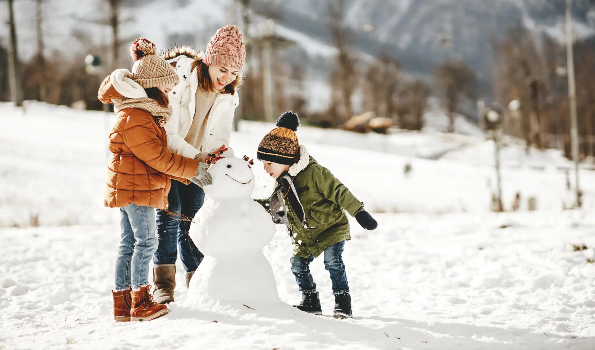 Family with hats builds a snowman near the Slow Travel Resort Kirchleitn – happy winter day on a family vacation in Bad Kleinkirchheim.