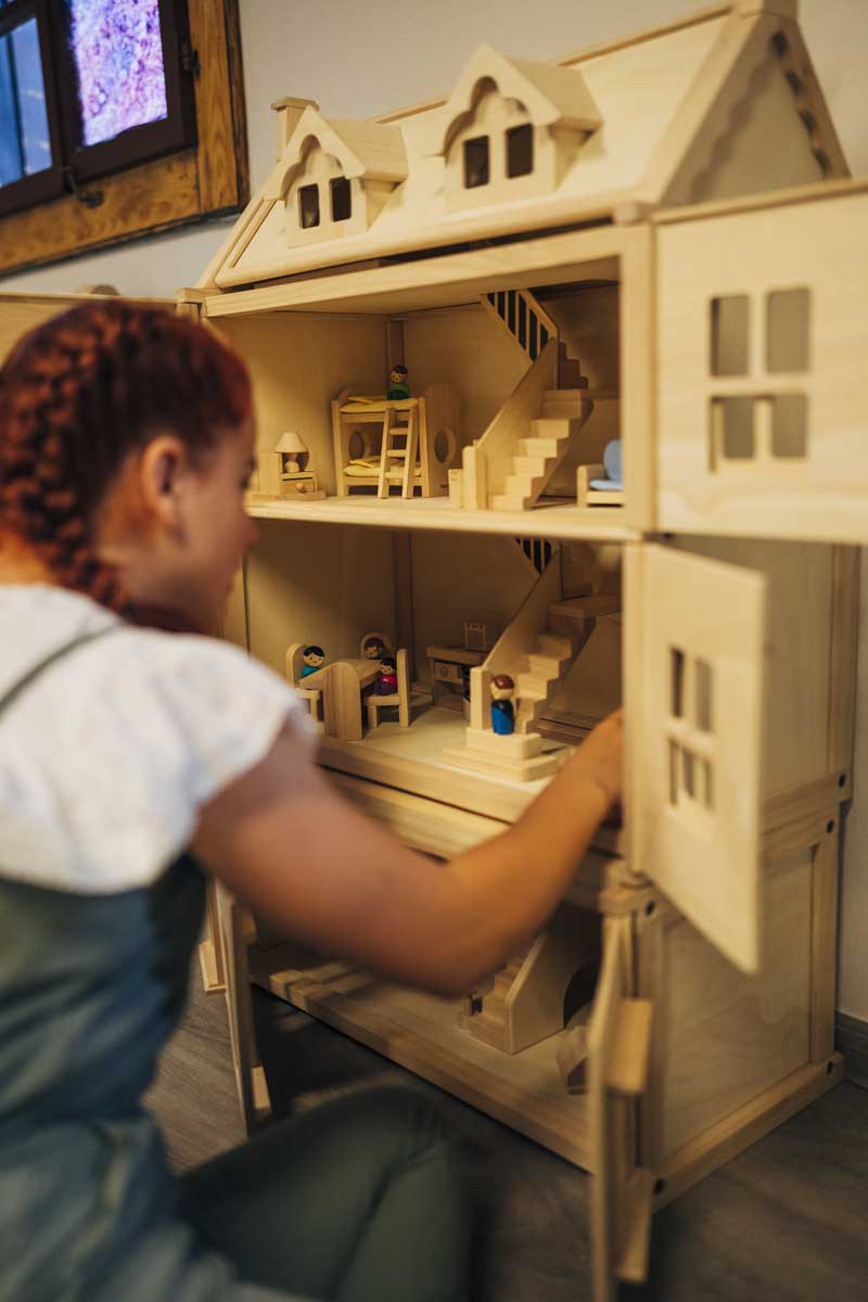 Casa delle bambole nell’area bambini interna Ragazza gioca con una casa delle bambole in legno nell'area bambini interna del villaggio vacanze Kirchleitn a St. Oswald