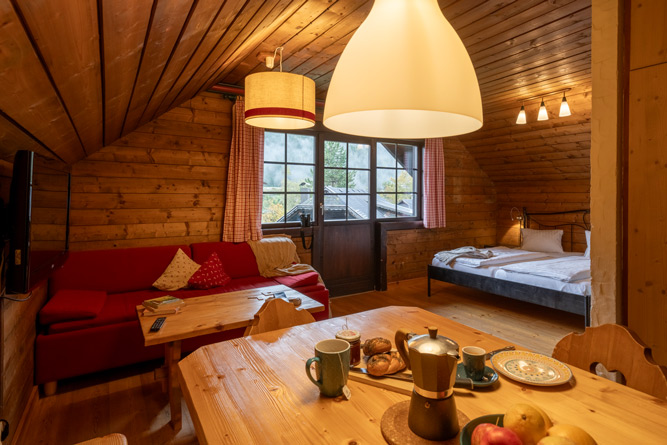 Gemütliche Stube im Appartement Rosennock im Slow Travel Resort Kirchleitn mit Essbereich, Sofa und Doppelbett – ideal für Familienzeit.