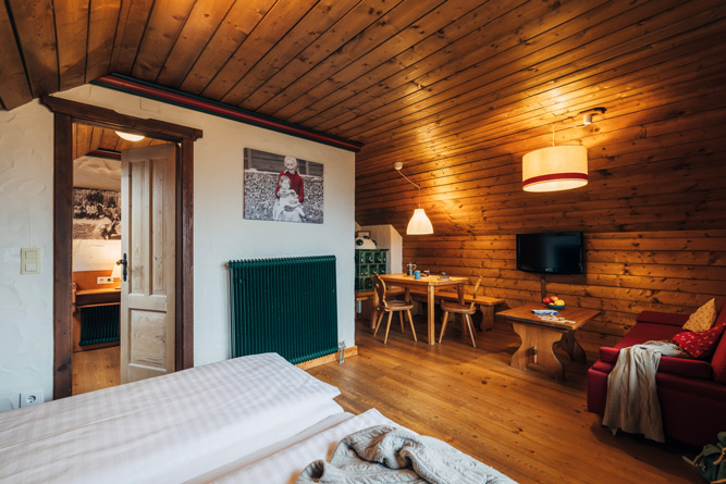 Blick vom Doppelbett auf Essecke, Sofa und Kachelofen im Appartement Rosennock im Slow Travel Resort Kirchleitn in Bad Kleinkirchheim.