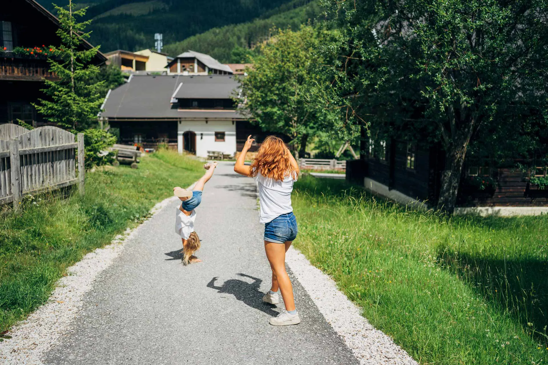 Zwei Mädchen schlagen Räder im Feriendorf Kirchleitn in Bad Kleinkirchheim, umgeben von alpinen Ferienhäusern und Natur.