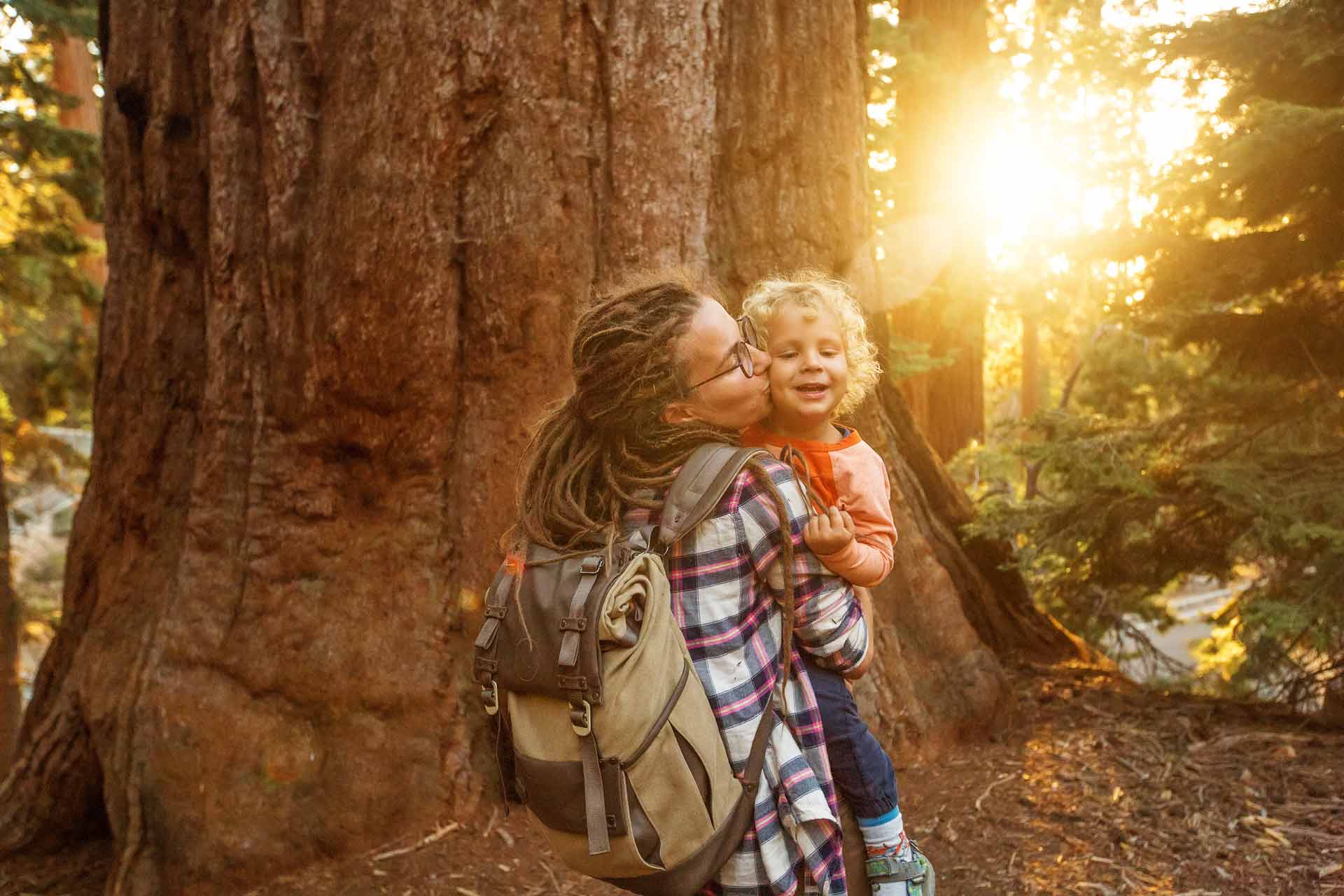 Mutter und Kind spazieren achtsam durch den Wald in Bad Kleinkirchheim, die Sonne scheint durch die Bäume.